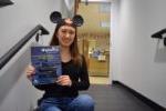 student wearing Mickey Mouse ears sits on a stair while holding a Disney internship flyer